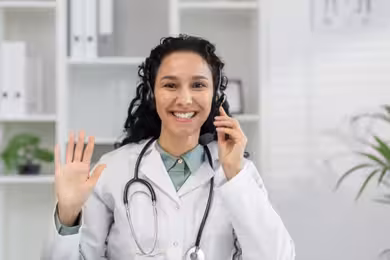 Physician smiling and waving at webcam wearing a headset